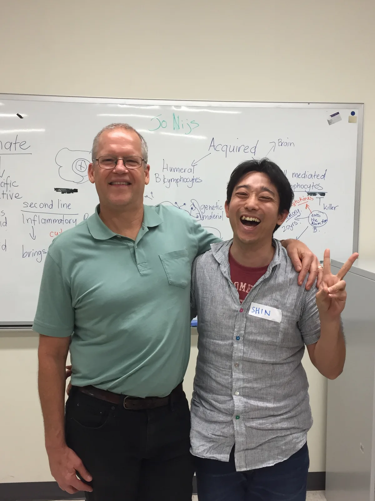 講義後のホワイトボードの前で、Mark Jones氏と笑顔で並ぶ木村晋一朗。ホワイトボードには痛みと免疫についての図が残っている