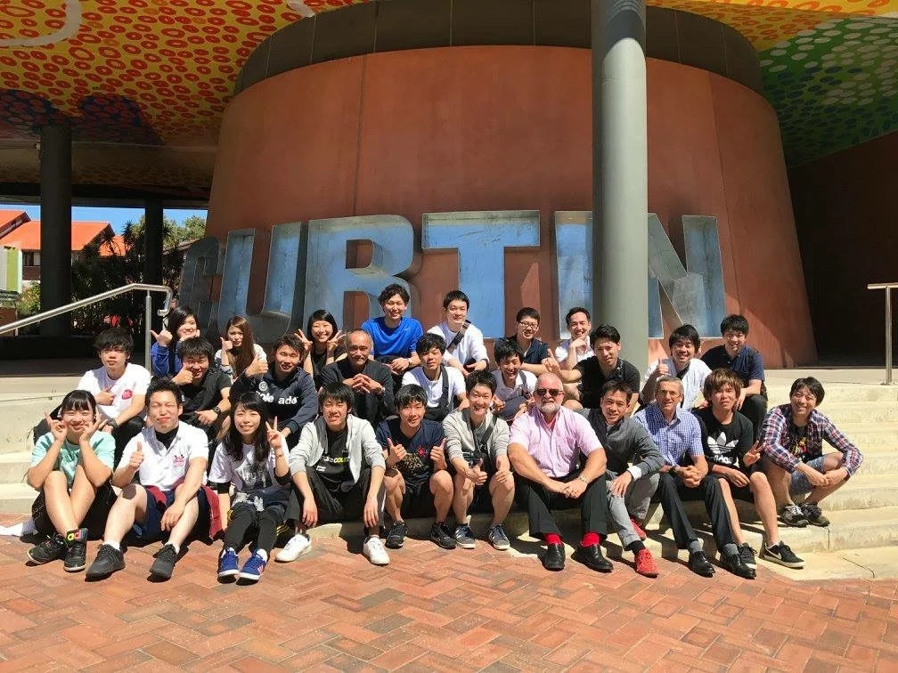 カーティン大学のCURTINモニュメント前での研修参加者の集合写真。前列にマリガンコンセプト指導者のトビー・ホール氏とキム・ロビンソン氏、通訳の成田崇矢先生、二列目に亀尾徹先生、前列右端に木村晋一朗